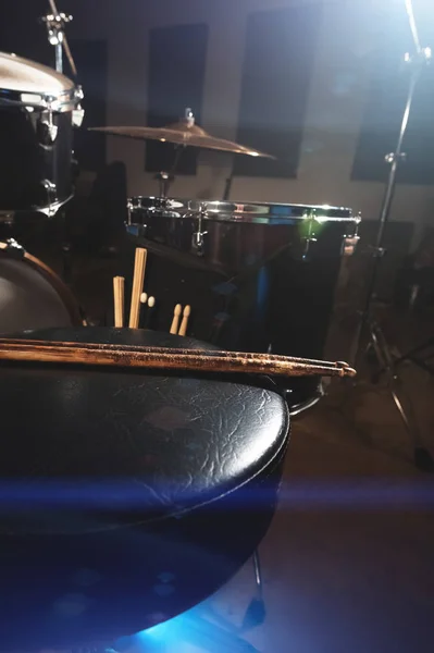 Close-up of used drumsticks lie on a drummers chair against the background of a drum kit and flare of spotlights. The concept of music — Stock Photo, Image