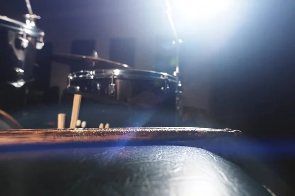Close-up of used drumsticks lie on a drummers chair against the background of a drum kit and flare of spotlights. The concept of music
