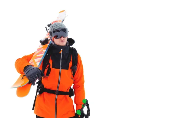 Portret van een professionele atleet skiër in een oranje jasje met een zwart masker en met ski's op zijn schouder kijkt in de camera. Geïsoleerd op wit — Stockfoto