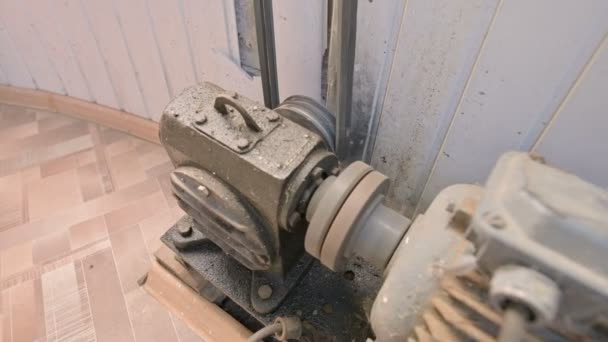An old electric motor covered with dust and dirt turns a two-thread pulley through a cardan gearbox with a belt drive to another mechanism. The concept of old electro engines and equipment — Stock Video