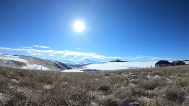 Timelapse dag flere huse på baggrund af snedækkede bjerge i Kaukasus med dannelsen af skyer i den klare himmel. Bevægelsen af solen i himlen – Stock-video