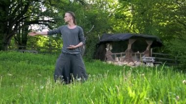 Genel plan Hint giysi ve pantolon Aladdin uygulamaları qigong genç bir adam eski bir kulübe 4k yanında yaz açık havada qi enerji ile çalışan egzersizleri yaparken