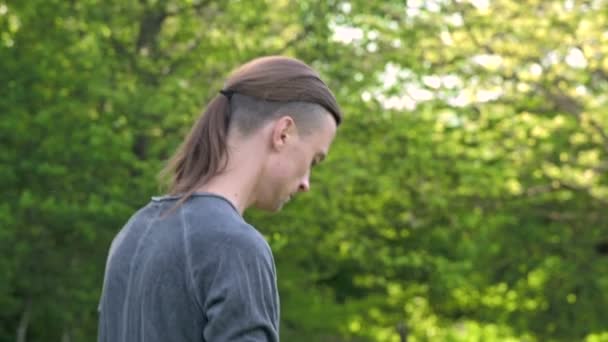 Close-up of a young man in indian clothes and pants alladin practicing qigong while doing exercises while working with qi energy outdoors in summer next to an old hut — Stock Video