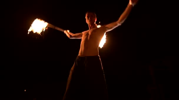 Пожарное шоу. Человек жонглирует двумя горящими факелами. Ночное шоу. Мастерство факира. Низкий угол — стоковое видео