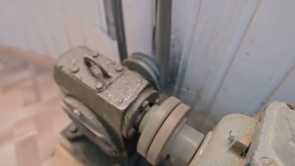 Un vieux moteur électrique recouvert de poussière et de saleté tourne une poulie à deux fils à travers une boîte de vitesses cardan avec un entraînement par courroie vers un autre mécanisme. Le concept des vieux moteurs et équipements électriques 