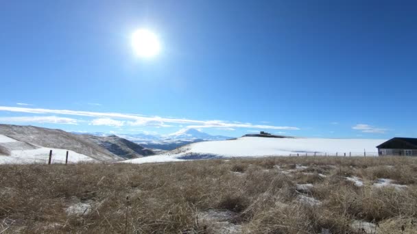 Zeitraffer Tag mehrere Häuser vor dem Hintergrund der schneebedeckten Berge des Kaukasus mit der Bildung von Wolken am klaren Himmel. die Bewegung der Sonne am Himmel — Stockvideo