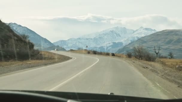 Θέα από το παρμπρίζ ενός αυτοκινήτου που οδηγεί κατά μήκος ενός ορεινού ασφαλτοστρωμένου δρόμου με φόντο όμορφα βουνά και σύννεφα — Αρχείο Βίντεο