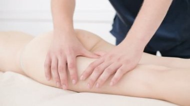 Yakın çekim bir erkek fizyoterapist pamuk bir delikanlı yanında profesyonel bir spa salonunda genç bir kadının kalça ve kalça ısınmak için hafif bir masaj yapıyor. 4k masaj vücut bakım konsepti