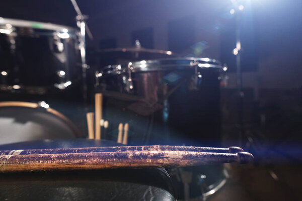 Close-up of used drumsticks lie on a drummers chair against the background of a drum kit and flare of spotlights. The concept of music