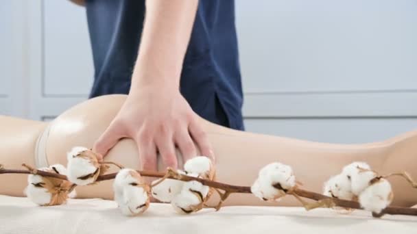 Nahaufnahme eines männlichen Physiotherapeuten, der einer jungen Frau vor Massageanwendungen in einem professionellen Wellness-Salon Massageöl auf den Oberschenkel und das Gesäß reibt. Konzept der Entspannung und Körperpflege in 4k — Stockvideo