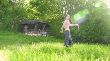 Uzun atış Uzun saçlı ve çıplak gövdeli genç bir adam dövüş sanatı konusunda eğitilir ve bir yaz sabahı açık havada rotasyonda bir personel veya yük halat ile konuşmadan önce. Düşük açı