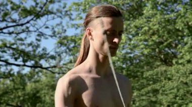 Bir yangın gösterisi için uzun saçlı bir adamın orta yakın çekim sabah eğitimi. Açık havada güneşli bir yaz sabahı meşaleler ve zincirler ile ateş olmadan bir performans için hazırlık