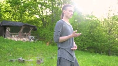 Ortalama bir plan Hint giysi ve pantolon Aladdin uygulamaları qigong bir genç adam eski bir kulübe yanında yaz aylarında qi enerji açık havada çalışırken egzersizleri yaparken