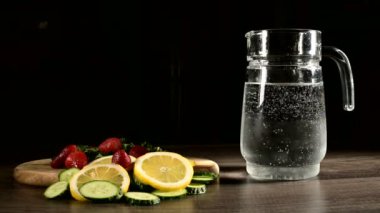 Cam karafe taze meyve ve köpüklü maden suyu limon nane ve salatalık ile dondurulmuş çilek ile karanlık bir arka plan üzerinde