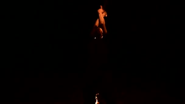 Пожарное шоу. Человек жонглирует двумя горящими факелами. Ночное шоу. Мастерство факира. Низкий угол — стоковое видео
