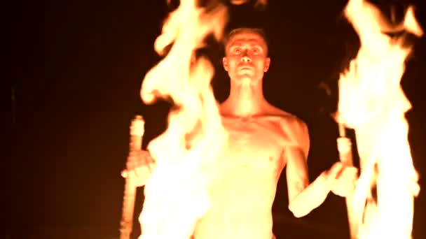 Пожарное шоу. Человек жонглирует двумя горящими факелами. Ночное шоу. Мастерство факира. Крупный план — стоковое видео