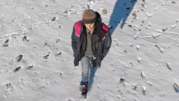 Het volgen van de mens in jeans en warme schoenen wandelen in het sneeuwveld op een winterse zonnige dag. Bovenaanzicht van boven — Stockvideo