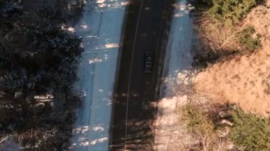 Güneşli bir günde iğne yapraklı bir kış ormanında asfalt yol boyunca sürüş bilinmeyen bir off-road araba havadan görünümü. Kış ulaşım konsepti. Düşük anahtar