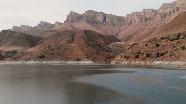 Vista aérea de un vuelo bajo sobre un lago congelado en invierno rodeado por las montañas del Cáucaso después del atardecer a la hora azul — Vídeo de stock