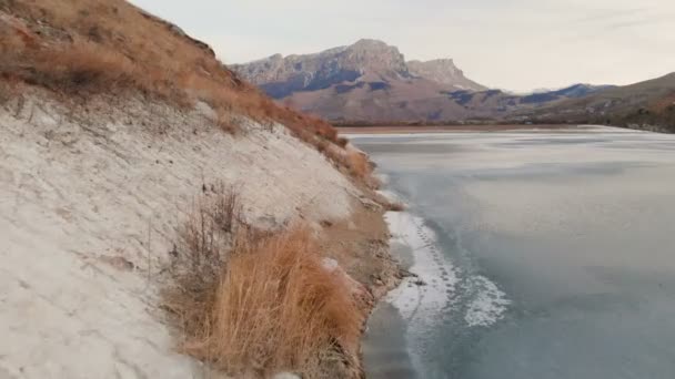 Vue aérienne d'un vol à basse altitude au-dessus d'un lac gelé en hiver entouré par les montagnes du Caucase après le coucher du soleil à l'heure bleue — Video