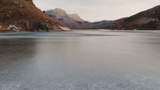 Vista aérea de un vuelo bajo sobre un lago congelado en invierno rodeado por las montañas del Cáucaso después del atardecer a la hora azul — Vídeo de stock