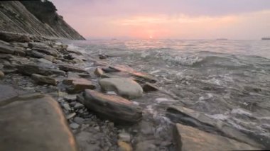 Yakın çekim yavaş hareket düşük geniş açı küçük deniz dalgaları kayalık bir plajda haddeleme. Sahil boyunca ileri ye doğru hareket edin. Sahil. Çakıl taşlı kayalık plajda akşam gün batımı