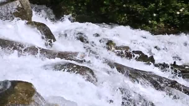 Piedras de primer plano y rociado de un río de montaña tormentoso en un bosque verde en cámara lenta con cableado de seguimiento. El concepto de calentamiento global y el problema de la cantidad de agua dulce en el planeta — Vídeo de stock