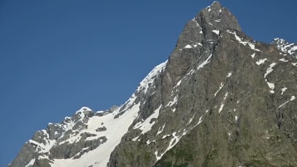 Close-up βίντεο Πανόραμα με τα χέρια των υψηλών βραχώδης βουνά του Καυκάσου με τα ερείπια του χιονιού το καλοκαίρι σε ένα καθαρό γαλάζιο του ουρανού — Αρχείο Βίντεο