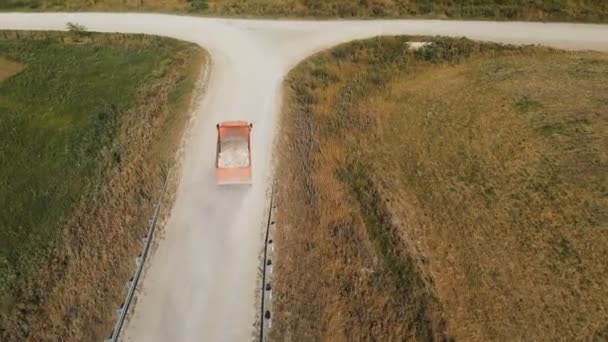 Vista aérea de un camión. Un camión volquete que transporta piedras de construcción y arena en un camión recorre un camino rural. Entrega de carga logística de camiones — Vídeo de stock