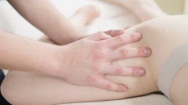 Yakın çekim bir erkek fizyoterapist pamuk bir delikanlı yanında profesyonel bir spa salonunda genç bir kadının kalça ve kalça ısınmak için hafif bir masaj yapıyor. 4k masaj vücut bakım konsepti