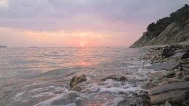 Yakın çekim yavaş hareket düşük geniş açı küçük deniz dalgaları kayalık bir plajda haddeleme. Sahil boyunca ileri ye doğru hareket edin. Sahil. Çakıl taşlı kayalık plajda akşam gün batımı