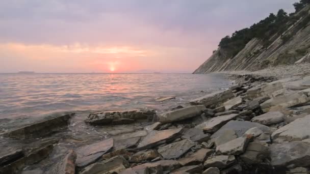 Close-up slow motion low grandangolo piccole onde marine che rotolano su una spiaggia rocciosa. Movimento lungo la spiaggia in avanti. Al mare. Tramonto serale su una spiaggia rocciosa di ghiaia — Video Stock