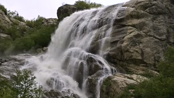 El agua en cámara lenta cae de una enorme roca. Cascada en el entorno natural en clima nublado con lluvia ligera — Vídeos de Stock