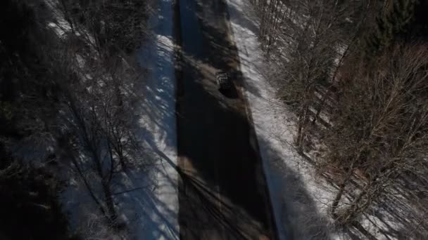 Widok z lotu ptaka nieznanego samochodu terenowego jazdy wzdłuż asfaltowej drogi w lesie iglastym zimą w słoneczny dzień. Koncepcja transportu zimą. Niski klucz — Wideo stockowe