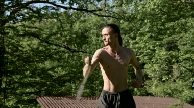 Bir yangın gösterisi için uzun saçlı bir adamın Sabah eğitim vurdu. Yeşil bir ormanın yanında açık havada güneşli bir yaz sabahı meşaleler ve zincirler ile ateş olmadan bir performans için hazırlık.