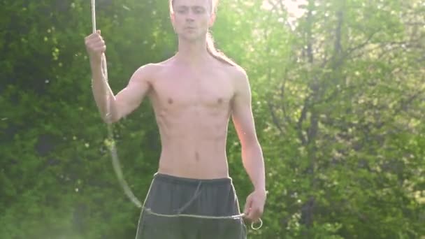 Střední záběr mladý muž s dlouhými vlasy a nahý trup je vycvičen v bojovém umění a předtím, než se v letním ránu vymluví s personálem nebo s lanem v rotaci venku. Nízký úhel — Stock video
