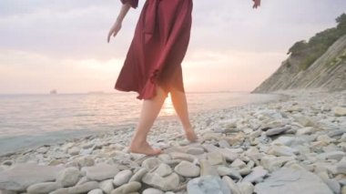 Gün batımında rüzgarda çırpınan kırmızı elbiseli yalınayak bir kızın bacaklarının arkasından ilerleyen yakın çekim yavaş hareket, deniz kıyısının taşları boyunca çömelerek yürüyor. Gelgitsizliğin Işık Anları