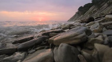 Yakın çekim yavaş hareket düşük geniş açı küçük deniz dalgaları kayalık bir plajda haddeleme. Sahil boyunca ileri ye doğru hareket edin. Sahil. Çakıl taşlı kayalık plajda akşam gün batımı