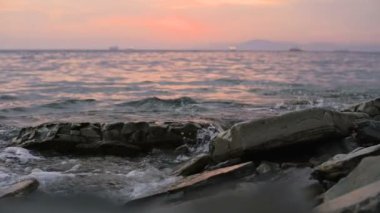 Yakın çekim yavaş çekim düşük açı küçük deniz dalgaları kayalık bir plajda haddeleme. Sahil. Çakıl taşlı kayalık plajda akşam gün batımı