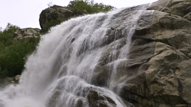 El agua en cámara lenta cae de una enorme roca. Cascada en el entorno natural en clima nublado con lluvia ligera — Vídeos de Stock