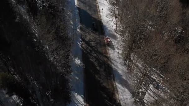 Widok z lotu ptaka nieznanego samochodu terenowego jazdy wzdłuż asfaltowej drogi w lesie iglastym zimą w słoneczny dzień. Koncepcja transportu zimą. Niski klucz — Wideo stockowe