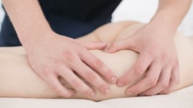 Yakın çekim bir erkek fizyoterapist pamuk bir delikanlı yanında profesyonel bir spa salonunda genç bir kadının kalça ve kalça ısınmak için hafif bir masaj yapıyor. 4k masaj vücut bakım konsepti