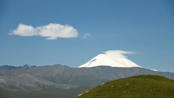 Středovýchodní krajina východního svahu hory ELBRUS. Formace v průzračném modrém nebi mraků nad zasněženou horou za letního slunného dne. Tvorba mraků změna počasí — Stock video