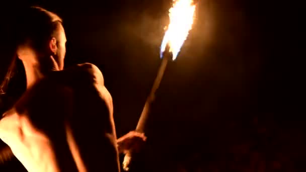 Primo piano Il rallentatore di un giovane uomo in pantaloni neri in totale oscurità mostra una rappresentazione di una torcia rotante accesa. Meditazione in movimento. Calmo e incrollabile. Lavora con il fuoco. Chiave bassa — Video Stock