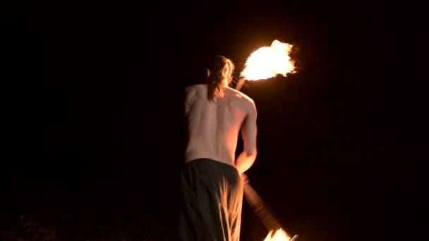 Le mouvement lent d'un jeune homme avec un torse nu en pantalon noir dans l'obscurité totale montre une représentation d'une torche brûlante rotative. Méditation en mouvement. Calme et inébranlable. Travaillez avec le feu. Clé basse — Video