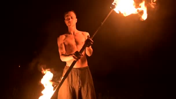 Slow motion of a young man with a naked torso in black pants in total darkness Combines two burning torches into one shows a representation of a rotating burning torch. Meditation in motion. — Stock Video