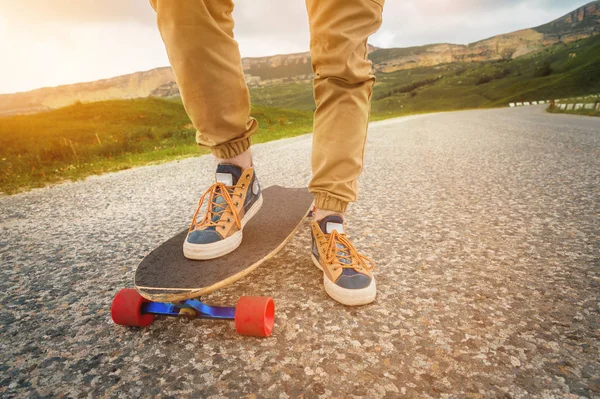 Güneş batımında asfalt arka planda bir Longboard üzerinde bez spor ayakkabıları erkek bacaklar yakın çekim. Erkek bacakları olan büyük bir kaykay. Gençlik eğlence konsepti — Stok fotoğraf