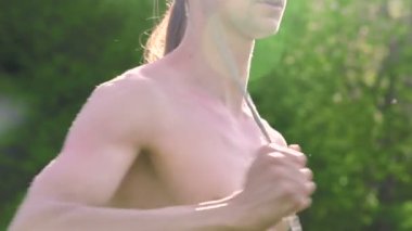 Uzun saçlı bir adamın gösteri için yakın çekim sabah eğitimi. Yeşil bir ormanın yanında açık havada güneşli bir yaz sabahı meşaleler ve zincirler ile ateş olmadan bir performans için hazırlık.