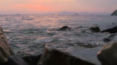 Yakın çekim yavaş çekim düşük açı küçük deniz dalgaları kayalık bir plajda haddeleme. Sahil. Çakıl taşlı kayalık plajda akşam gün batımı