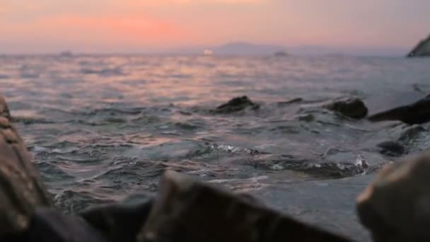 Close-up câmera lenta de baixo ângulo pequenas ondas do mar rolando em uma praia rochosa. À beira-mar. Pôr do sol à noite em uma praia rochosa de seixos — Vídeo de Stock